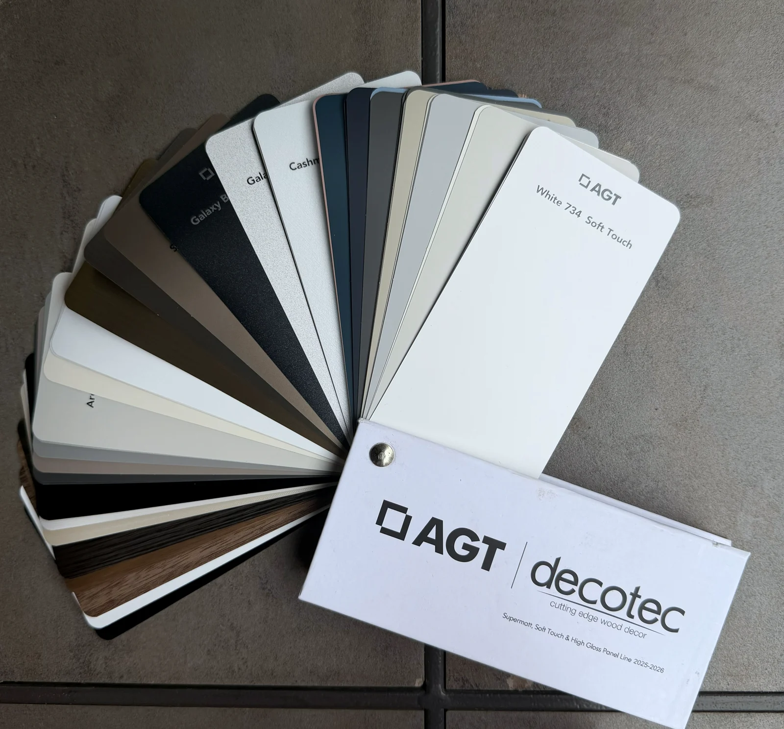 AGT decotec panel samples fanned open, showing the supermatte and soft-touch range in whites, greys, black and two woodgrains