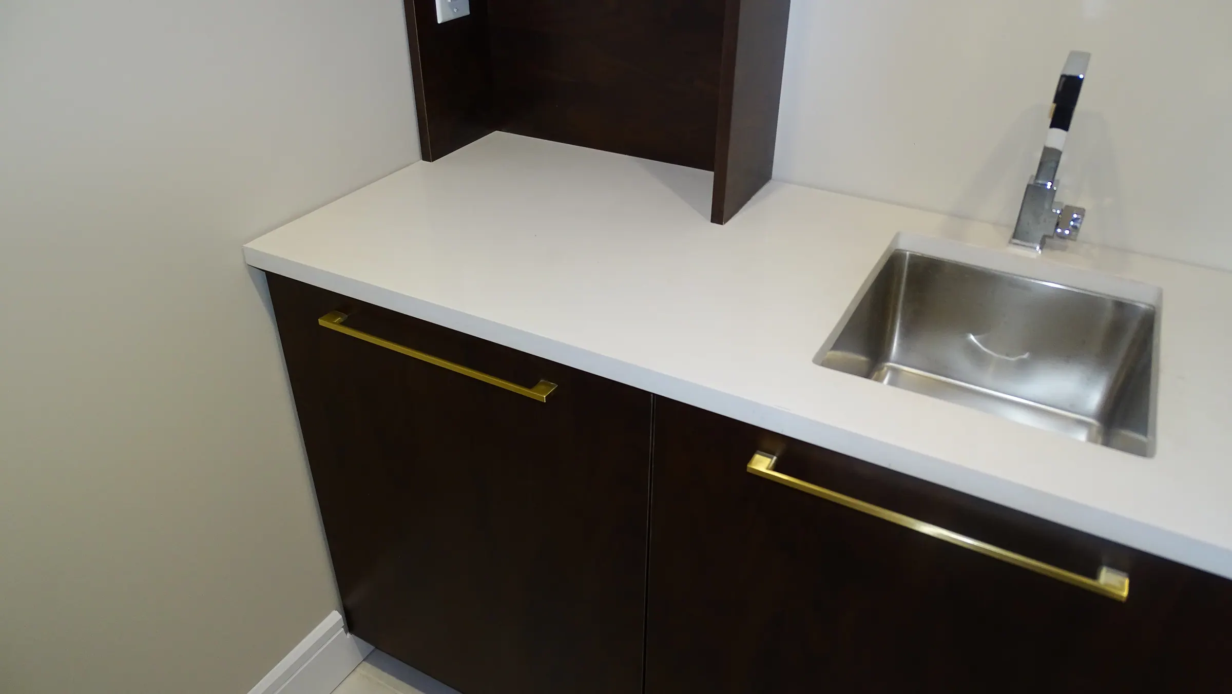 Bar counter in white quartz with an inset stainless sink, over espresso base cabinets on long brass bar pulls